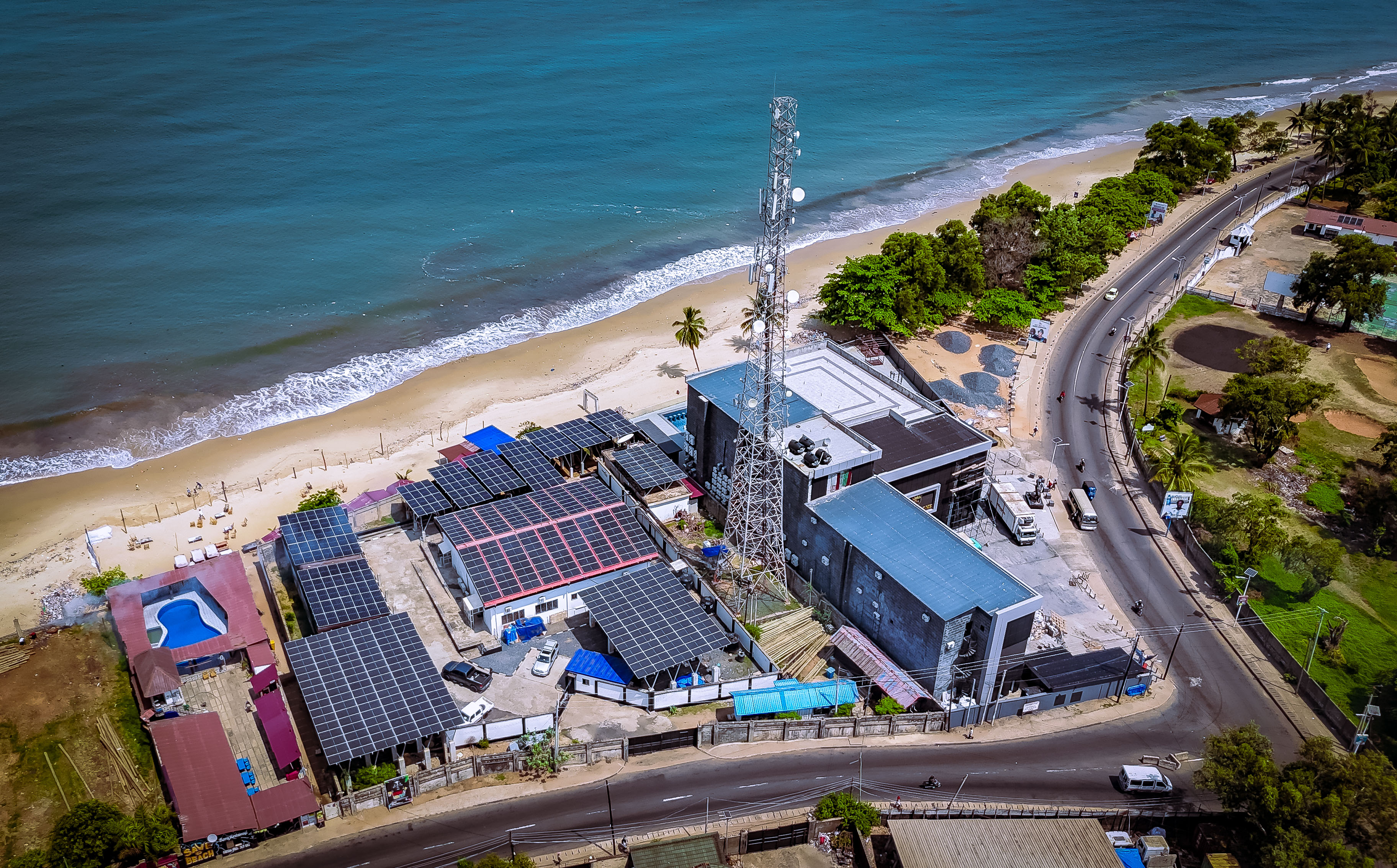 A birds-eye view of the beach at Freetown, Sierra Leone, with a telecom tower and data centre, surrounded by solar panels.
